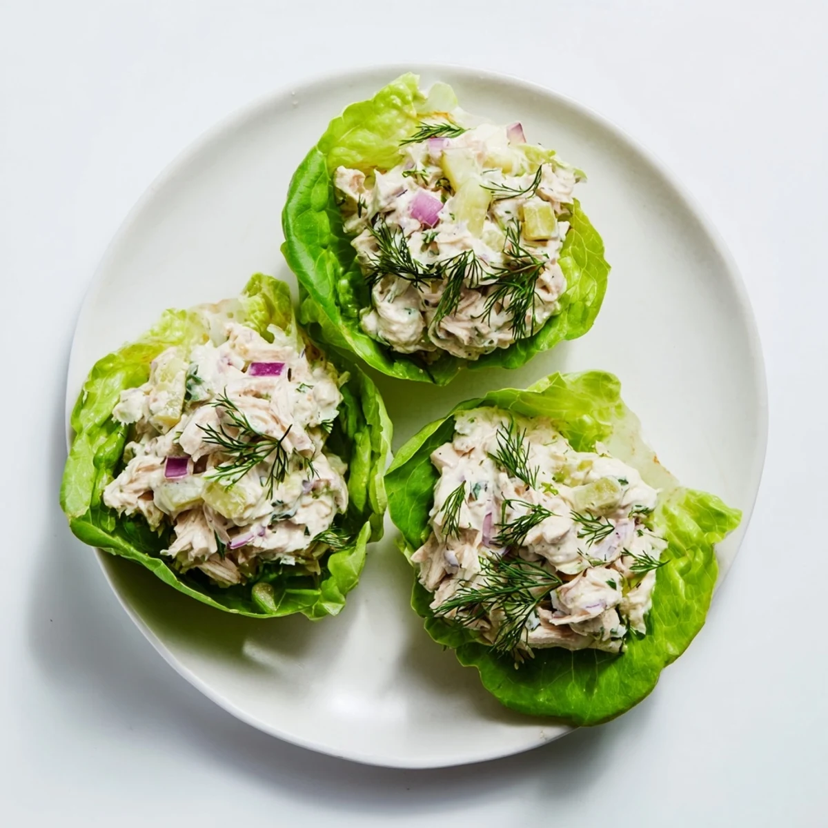 A close-up of Dill Pickle Chicken Salad Lettuce Cups, showcasing creamy chicken salad with crunchy pickles and red onion nestled in crisp green lettuce leaves.