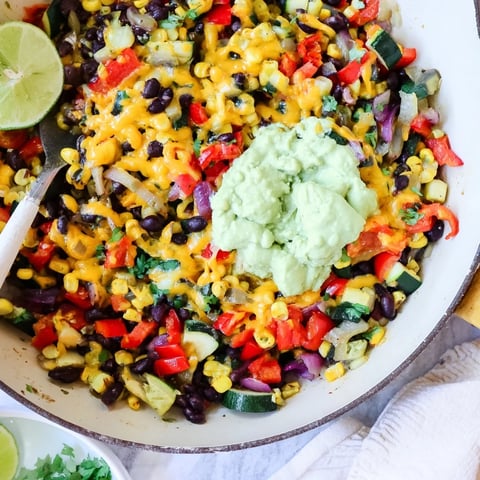 Steaming Veggie-Packed Taco Skillet with Avocado Yogurt topped with fresh cilantro and a lime wedge.