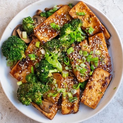 Golden, crispy-edged Sautéed Tofu Steak beside vibrant broccoli and mushrooms in savory sauce.
