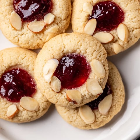 Golden, buttery Cherry Almond Thumbprint Cookies, perfect for dessert, filled with vibrant red cherry jam.