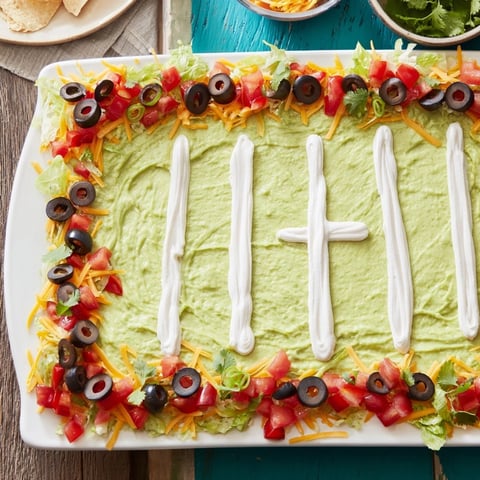 Vibrant football field dip platter, layered with cheese and fresh toppings, ready for dipping chips.