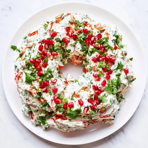 A creamy, vibrant Red Pepper and Spinach Dip Wreath, garnished with parsley and bright pomegranate seeds.