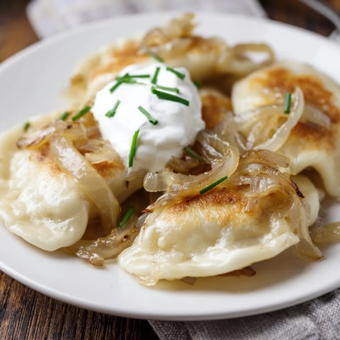 Golden-brown pan-fried Polish pierogi dumplings are served with sweet caramelized onions and creamy sour cream.