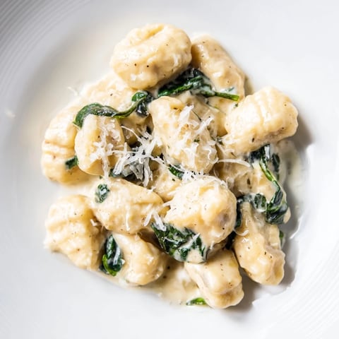 Creamy Garlic Gnocchi in a rich, velvety garlic cream sauce with wilted spinach on a rustic plate.