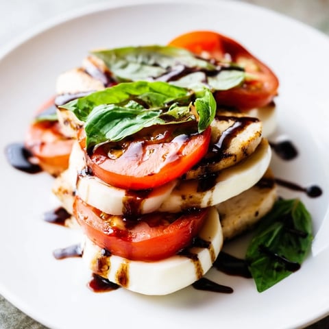 Grilled chicken slices rest atop fresh mozzarella, ripe tomatoes, and basil in this vibrant Chicken Caprese Salad, drizzled with balsamic.