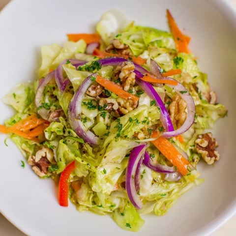 A warm and vibrant Cooked and Loved Cabbage Salad with sautéed cabbage, julienned carrots, and red bell peppers glistening with a tangy apple cider vinaigrette in a rustic serving bowl.