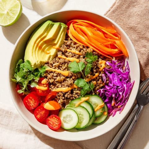Hearty plant-based meat bowl garnished with avocado, cucumber, and spicy mayo sauce.  