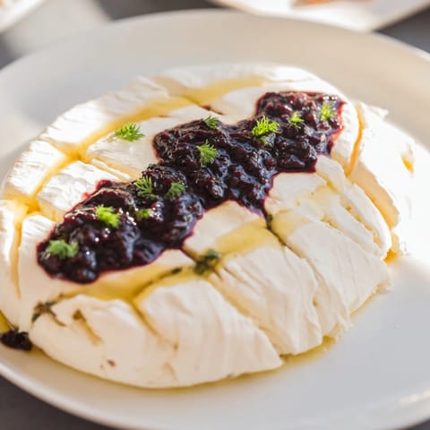 A close-up of The Victorian Cameo: artistic black olive tapenade atop creamy cheese with fresh herbs.