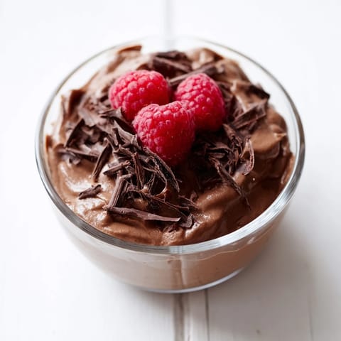 A close-up of creamy avocado chocolate pudding, garnished with fresh raspberries and shaved dark chocolate.