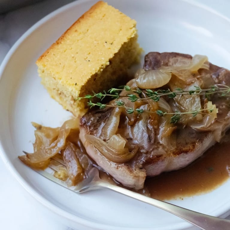 Imagine juicy Smothered Pork Chops & Cornbread! See the tender pork with golden cornbread, immersed in rich gravy.