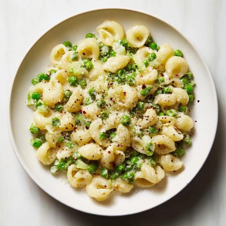 Close-up of golden Macaroni & Peas, tossed with peas and Parmesan cheese.