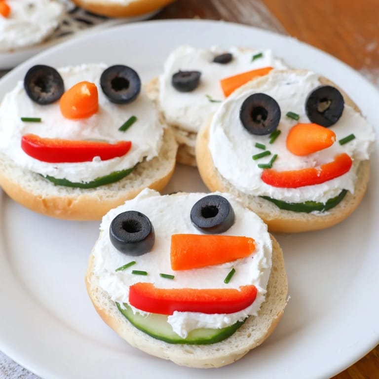 Delicious Snowman Mini Bagel Sandwiches feature carrot noses and cucumber scarves, perfect for a fun winter meal.